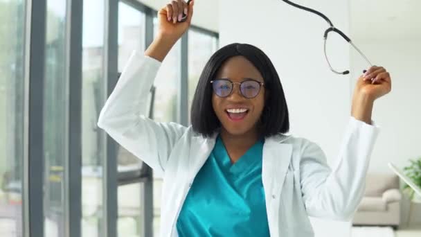 Happy young african american woman doctor dancing with a stethoscope in the hospital - Filmmaterial, Video