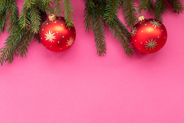Εορταστικό κλαδί πεύκου με κόκκινες χριστουγεννιάτικες διακοσμήσεις σε ροζ φόντο. Επίπεδο lay, πάνω όψη. - Φωτογραφία, εικόνα