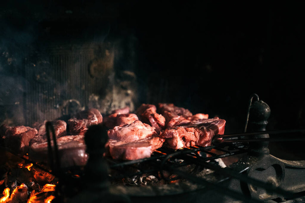 Ψητό κρέας στο τζάκι του σπιτιού του. Ωμό βόειο κρέας σε σχάρα μπάρμπεκιου με τα κάρβουνα από κάτω. - Φωτογραφία, εικόνα