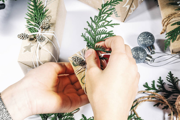 Το παιδί τυλίγει χειροποίητα χριστουγεννιάτικα δώρα σε χαρτί χειροτεχνίας με κλαδιά χριστουγεννιάτικων δέντρων και κώνους Το παιδί ετοιμάζει δώρα για τον εορτασμό της Πρωτοχρονιάς. Ειρηνική δραστηριότητα αναψυχής πριν από τις χειμερινές διακοπές. - Φωτογραφία, εικόνα