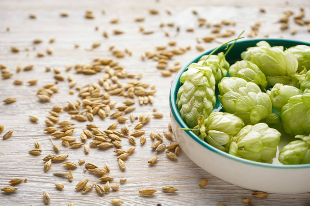 Fresh hops in a bowl and barley on a wooden background, close-up. - Photo, Image