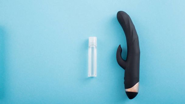 Top view of a black clitoral vaginal vibrator and a tube of lubricant on a blue background - Foto, immagini