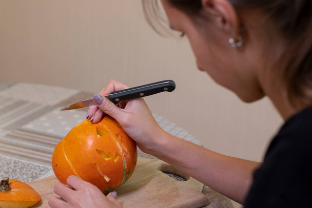 the process of making a Halloween pumpkin. cutting out the mouth by brunette girl. horror theme and Halloween - Foto, imagen