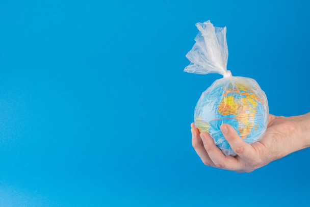 Hand holding planet earth inside a plastic bag over blue background with room for text. - Foto, imagen
