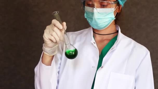 Médecins en uniforme, masque facial et lunettes regardant l'élément chimique liquide coloré dans la verrerie - Séquence, vidéo