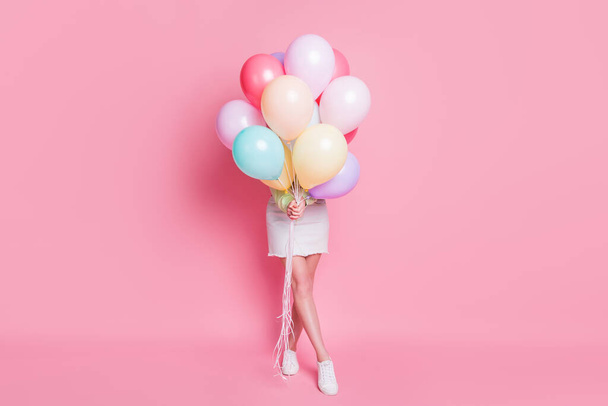 Full size photo of funny lady come birthday party hold many air balloons hiding face surprise visit wear casual green crop pullover jeans skirt shoes isolated pink pastel color background - 写真・画像