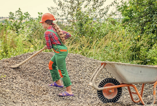Outdoor activity. girl who is transporting rubble in a wheelbarrow. construction work. girl builder takes a shovel of rubble. hardworking youth. game of builder and construction - Foto, imagen