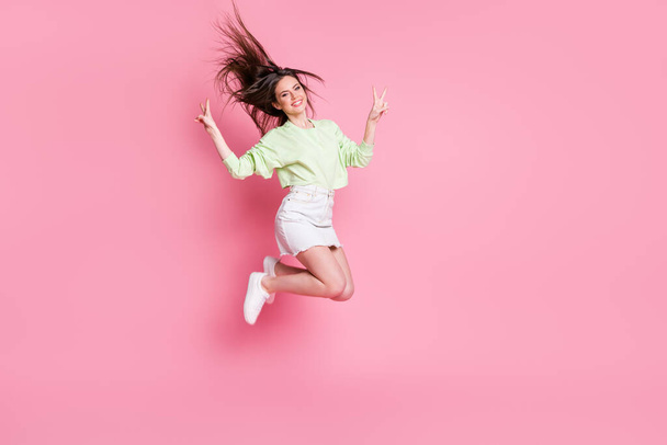 Full length profile photo of attractive youngster lady jumping high showing v-sign symbols wear casual crop pullover naked belly skirt shoes isolated pink color background - Photo, Image