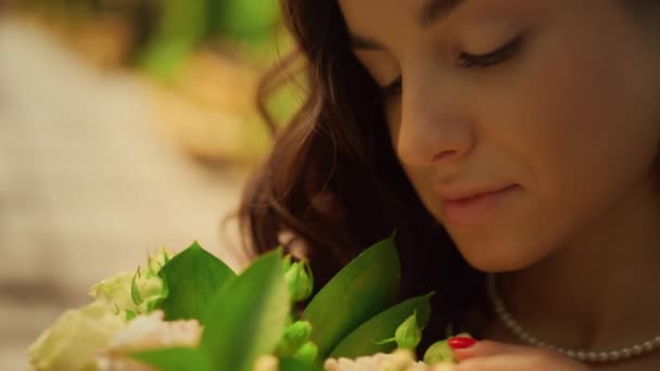 Beautiful bride admiring flowers in garden. Woman touching flower petals in park - Filmati, video