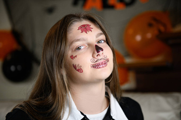 Tyttö näyttää itselleen Halloween meikki Santa Muerte tai sokeri Meksikon kallo. Halloween juhlitaan kotona - Valokuva, kuva