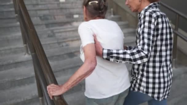 Zapewnianie pomocy i wsparcia osobom starszym. Babcia, pacjentka. Kobieta pomaga babci wspinać się po schodach. Starsza kobieta z opiekunką. Pielęgniarka wspomagająca, pomagająca starszej kobiecie wejść na schody - Materiał filmowy, wideo