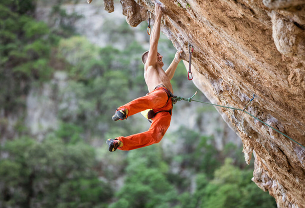 Young male rock climber after jumping and gripping small handholds on overhanging cliff - Photo, Image