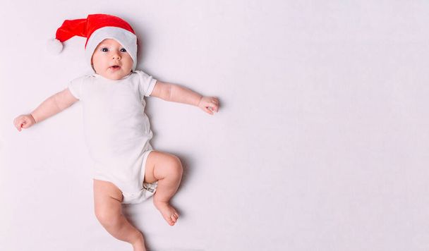 Симпатичный малыш в шляпе Санты на мягкой ткани. Первое рождество для ребенка. Малыш Санта. Новогодние праздники. - Фото, изображение