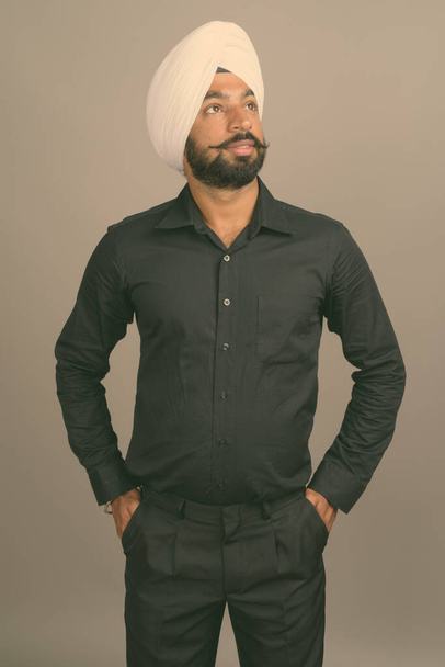 Young handsome Indian Sikh businessman wearing turban against gray background - Φωτογραφία, εικόνα