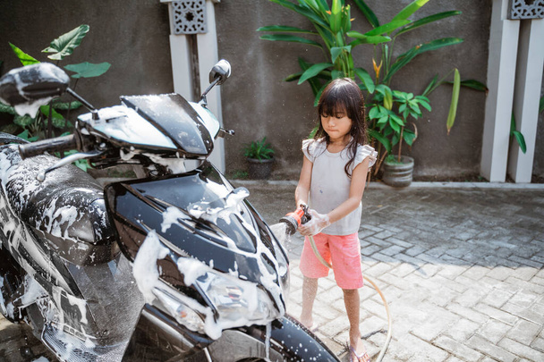 азиатская маленькая девочка моет свой мотоцикл водой - Фото, изображение