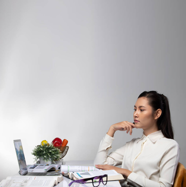 Fiatal ázsiai nő fehér ing gondol stressz, keményen dolgozik, könyveket olvasni, videokonferencia online az asztalon. Koncepció a top copy space üres üres területtel - Fotó, kép