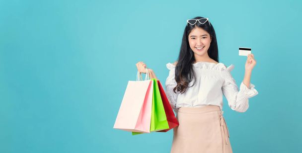 Veselé krásné asijské žena drží multi barevné nákupní tašky a kreditní karty na světle modrém pozadí. - Fotografie, Obrázek
