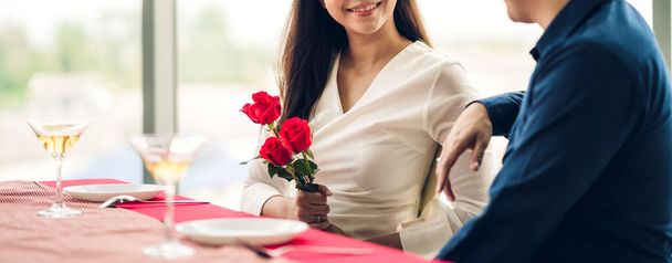 Молодой красивый мужчина дарит девушке сюрприз с красной розой и держит красную розу в День Святого Валентина дома - Фото, изображение