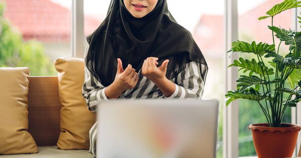 Молодая улыбающаяся красивая мусульманка расслабляется с помощью ноутбука компьютерной работы и видео-конференции встречи на home.work от дома концепции - Фото, изображение