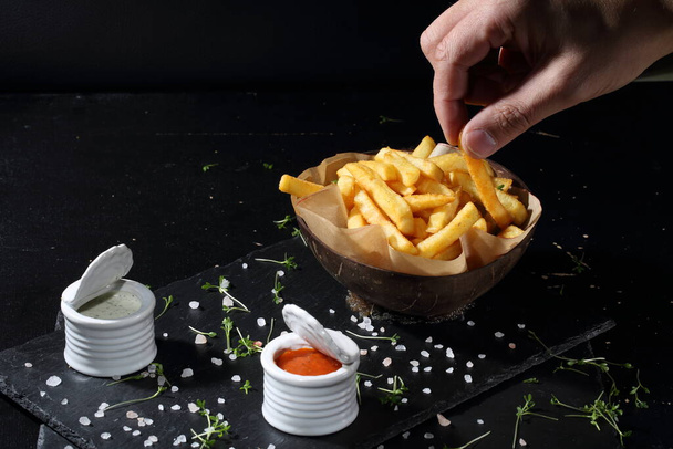 The hand takes the French fries. French fries on black background - 写真・画像