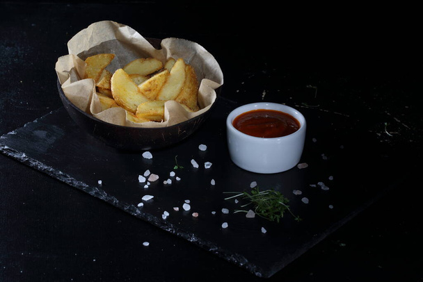 Rustic potatoes on a black background. Country style potatoes with sauce - Zdjęcie, obraz