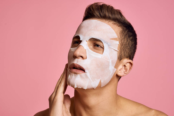 man with cleansing mask against black dots on his face on pink background cropped view and hands near face - 写真・画像