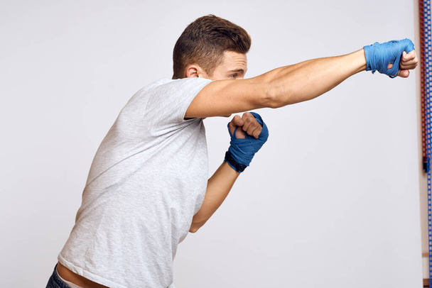 Sportlicher Boxer in blauen Handschuhen, der Schläge vor hellem Hintergrund übt - Foto, Bild