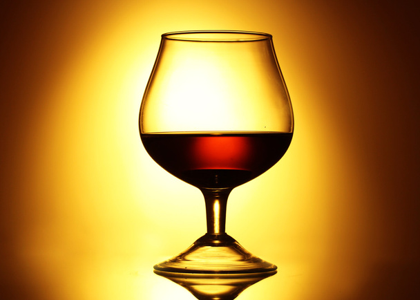 Glass of cognac on yellow background - Фото, изображение