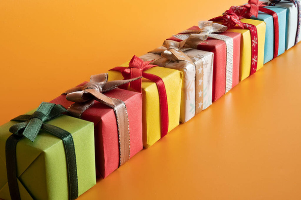 A closeup of multi-colored diagonally placed gift boxes in the orange background, Christmas mood - Φωτογραφία, εικόνα