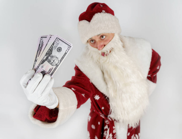 Πρωτοχρονιά και Χριστούγεννα. Ο Άγιος Βασίλης κρατάει χρήματα στα χέρια του. Απομονωμένα σε φωτεινό φόντο - Φωτογραφία, εικόνα