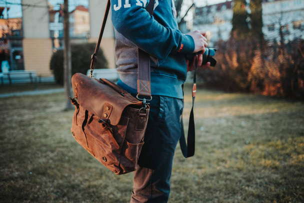 A closeup shot of a photographer holding a camera and a bag - Fotoğraf, Görsel