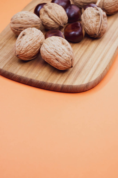 A shot of chestnuts and walnuts on a wooden board - Fotografie, Obrázek