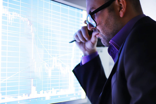 A businessman is looking at a graph on a monitor. An exchange broker evaluates stock market trends. A man with glasses in front of a curve of the dynamics of economy. - Photo, Image