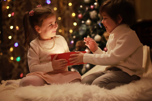 Famille le soir de Noël à la cheminée. Les enfants ouvrent des cadeaux de Noël. Enfants sous l'arbre de Noël avec des boîtes-cadeaux. Salon décoré avec cheminée traditionnelle. Cozy chaude maison de soirée d'hiver. - Photo, image