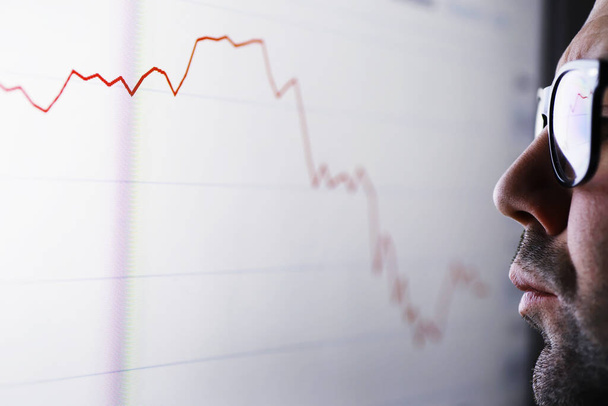Egy üzletember egy grafikont néz a monitoron. Egy tőzsdei bróker értékeli a tőzsdei trendeket. Egy szemüveges férfi a gazdaság dinamikájának görbülete előtt.. - Fotó, kép