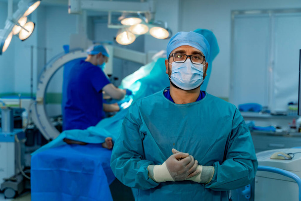 Medic in blue scrubs wearing face mask, glasses and latex gloves. Operating theatre. Modern surgery equipment. - Foto, immagini
