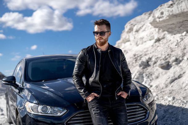 Attractive guy in fashion clothes travels by auto. Luxury car and white rocks background. - Foto, immagini