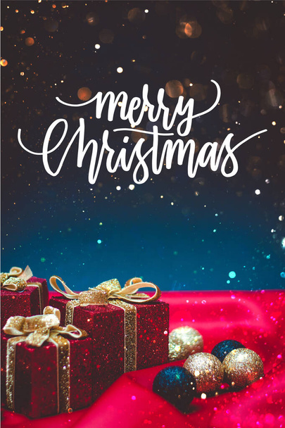 Primer plano de unas brillantes cajas de regalo rojas con luces y decoraciones navideñas sobre un fondo rojo y azul con la cita de Feliz Navidad - Foto, Imagen