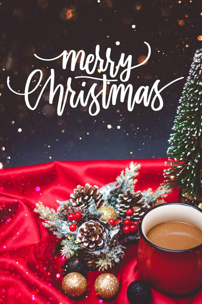 Φρέσκος και ζεστός καφές σε κόκκινο κύπελλο με χριστουγεννιάτικα φώτα και διακοσμήσεις σε κόκκινο και μαύρο φόντο με λάμψη και Καλά Χριστούγεννα απόσπασμα - Φωτογραφία, εικόνα