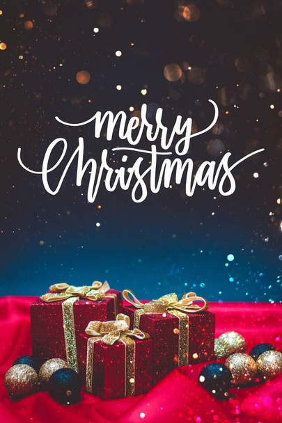 Caixas de presente vermelho brilhante com luzes de Natal e decorações em um fundo vermelho e azul com citação Feliz Natal - Foto, Imagem