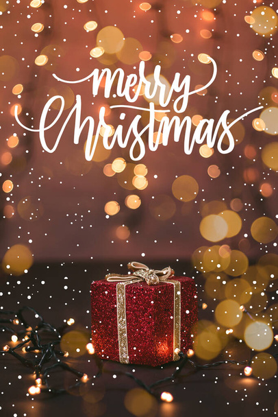 Фото красивої червоної блискучої подарункової коробки, боке світло і сніг з різдвяною цитатою
 - Фото, зображення