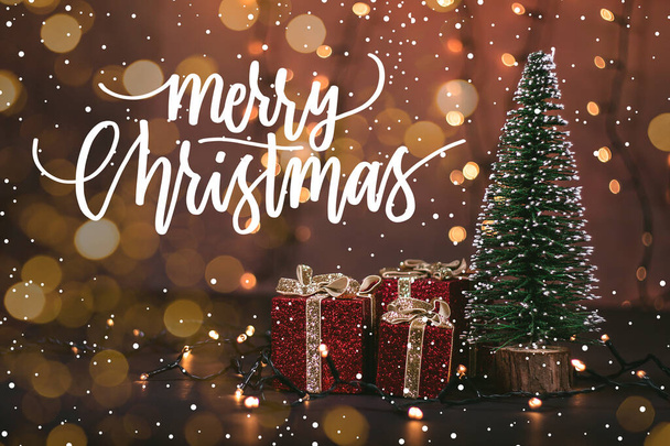 Foto de uma árvore de Natal com belos presentes embrulhados, luzes bokeh e neve com a citação de Natal - Foto, Imagem