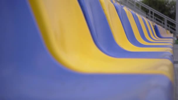 4k, linhas vazias de assentos de plástico no estádio. Assentos Amarelos e Azuis na Tribuna da Arena de Esportes sem Espectadores e Fãs - Filmagem, Vídeo