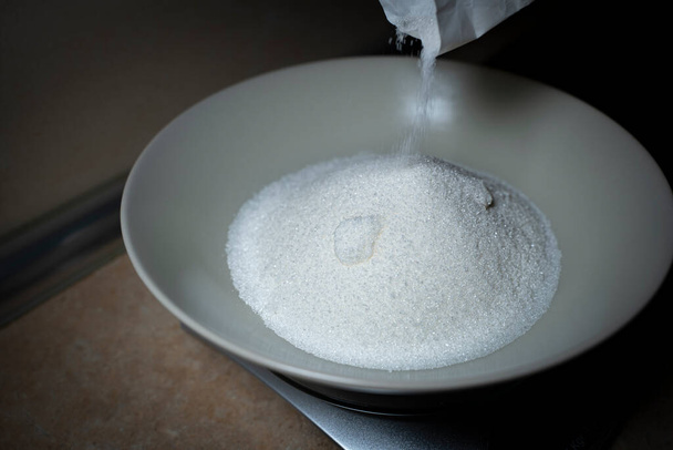 Ρίχνουμε ζάχαρη σε ένα βαθύ πιάτο. Υψηλή γωνία. - Φωτογραφία, εικόνα