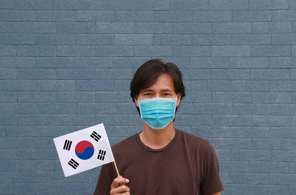 Чоловік у масках у коричневій сорочці та південнокорейський прапор у руці. Концепція захисту і боротьби з COVID 19. - Фото, зображення