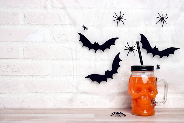 Orange Halloween cocktail in skull glass jars with cobwebs and bats. Copy space for text. - Foto, Bild