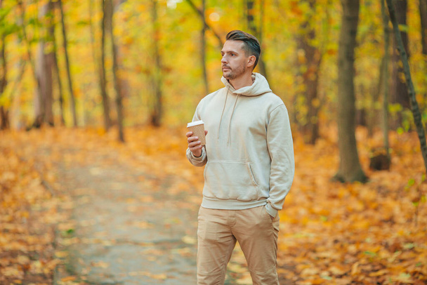 Young man drinking coffee in autumn park outdoors - Fotoğraf, Görsel