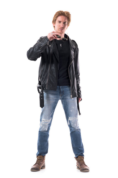 Confident assertive young stylish rocker or biker removing sunglasses looking at camera. Full body isolated on white background. - Photo, Image