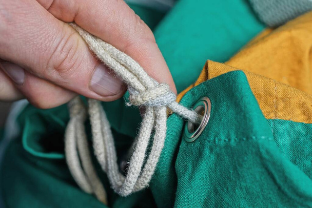 пальцы завязывают белый веревочный узел на цветном рюкзаке - Фото, изображение