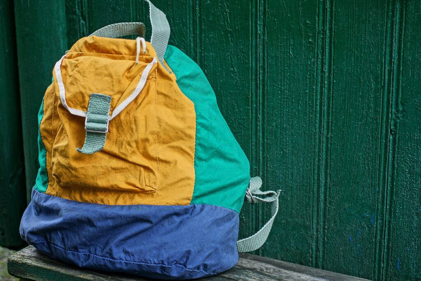un grand sac à dos pleine couleur se dresse contre un mur en bois vert à l'extérieur - Photo, image